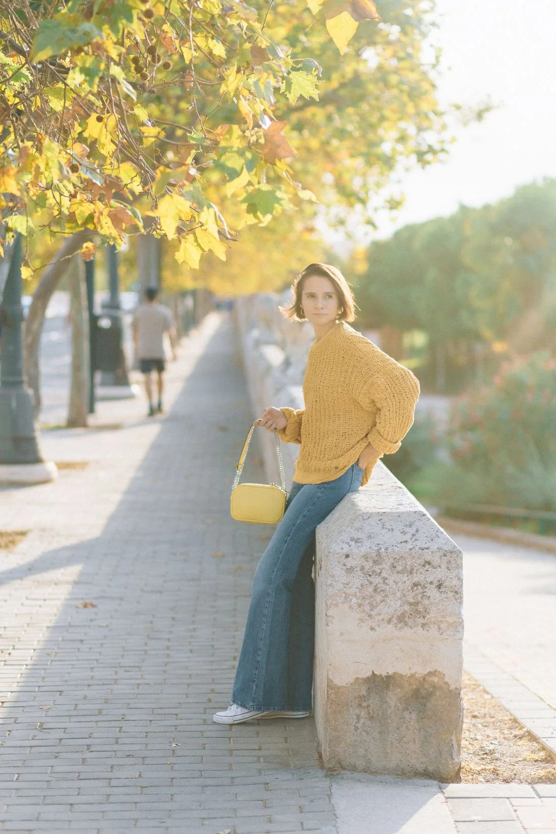 Woman wearing a knitted sweater and jeans on a sunny sidewalk