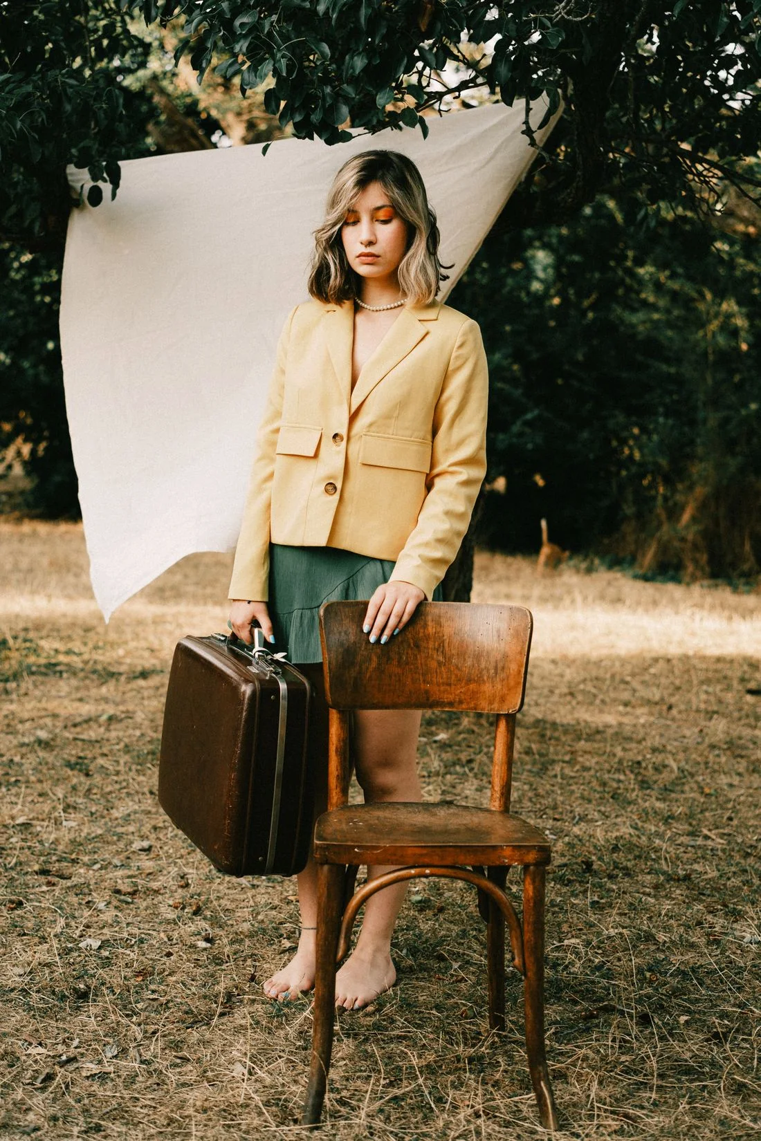 Woman wearing a yellow blazer and carrying a suitcase outdoors