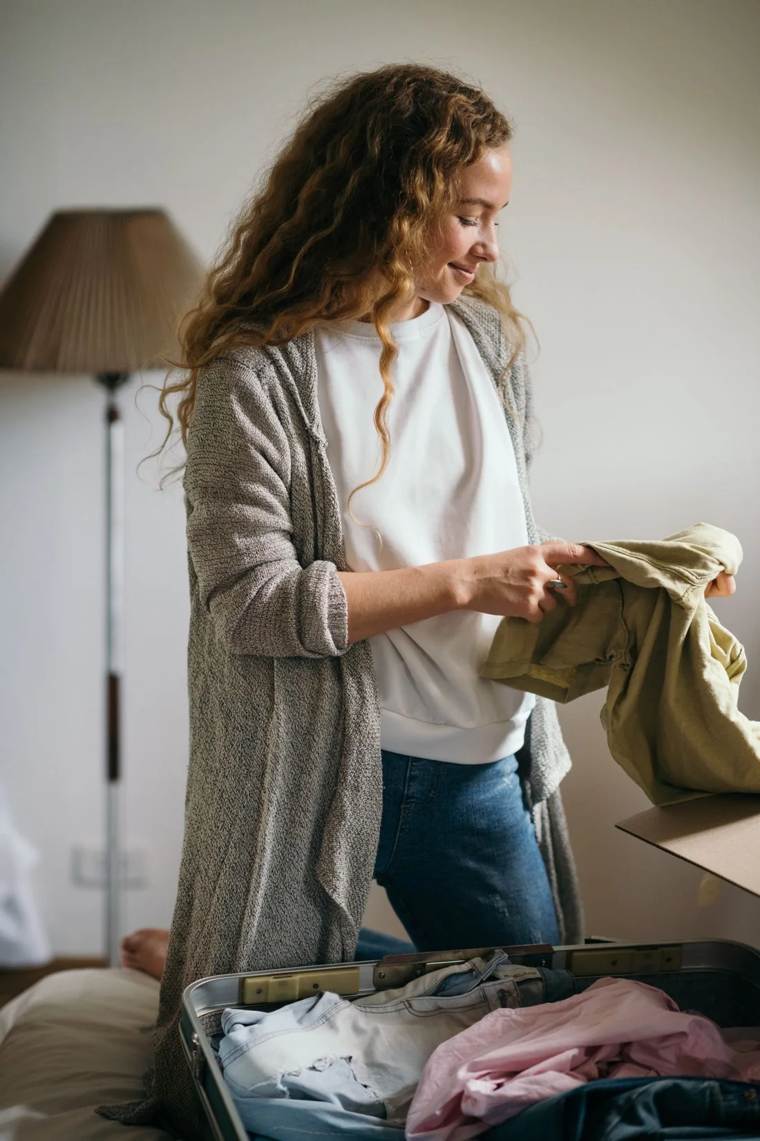 Woman arranging clothing inside a suitcase in a bedroom